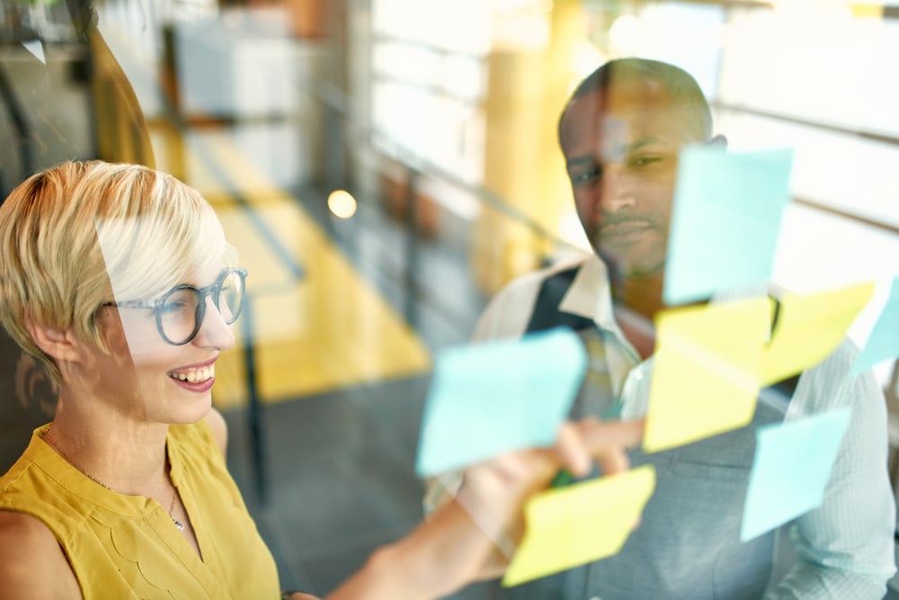 Two creative millenial small business owners working on social media strategy brainstorming using adhesive notes in windows-1